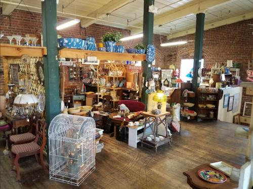A cozy antique shop filled with various vintage items, furniture, and decor, featuring exposed brick walls and wooden beams.