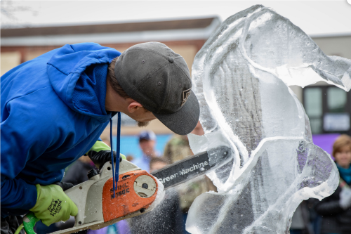 A person carves an ice sculpture using a chainsaw, focused on the intricate details of the ice.