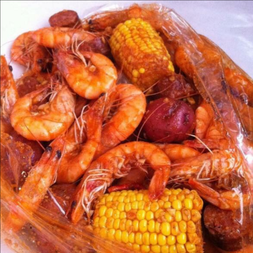 A seafood boil featuring shrimp, corn, sausage, and potatoes in a flavorful sauce, served in a plastic bag.