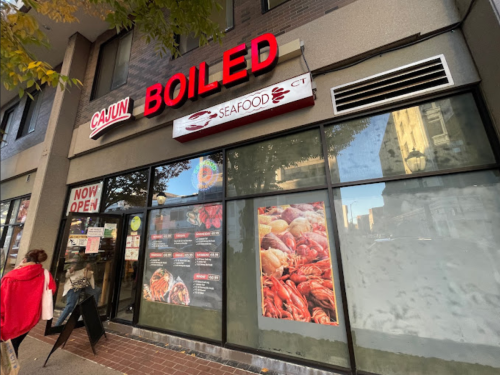 Exterior of Cajun Boiled restaurant with large red signage, showcasing seafood dishes and a "Now Open" sign.