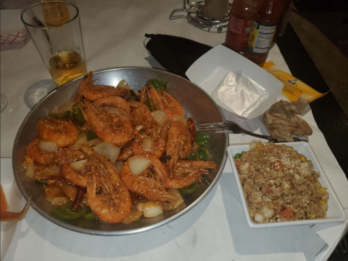 A large platter of spicy shrimp with vegetables, accompanied by a bowl of fried rice and a drink.