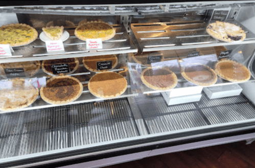 A display case filled with various pies, including chocolate, pecan, and fruit varieties, all labeled.