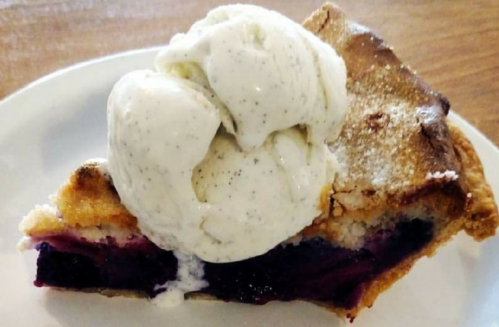 A slice of pie with a scoop of vanilla ice cream on top, featuring a rich berry filling and a golden crust.