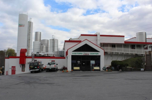A building labeled "Visitors Center" with silos in the background, surrounded by vehicles and greenery.