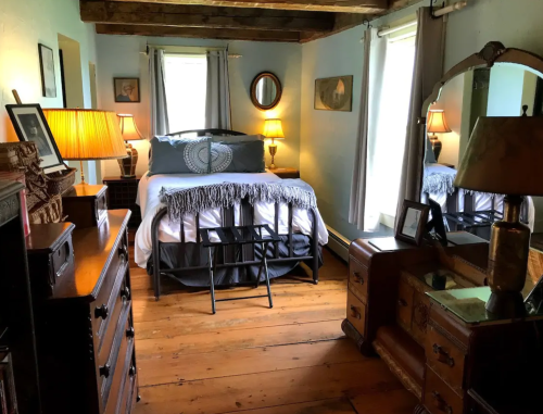 Cozy bedroom with a bed, wooden furniture, lamps, and a mirror, featuring rustic decor and warm lighting.