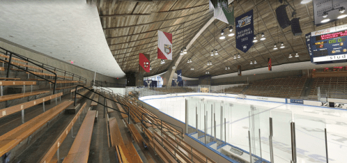 Interior view of a hockey rink with empty bleachers, banners hanging, and an ice surface ready for a game.
