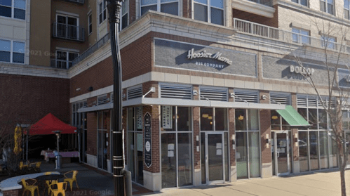 Exterior view of a restaurant with a sign reading "Hoosier Mama Pie Company," featuring outdoor seating and nearby buildings.