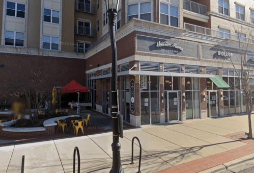 A restaurant with large windows, outdoor seating, and a red tent, located in a brick building.