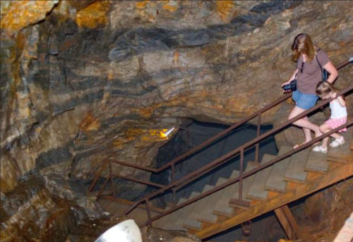 A woman and a child descend a metal staircase inside a cave, surrounded by rocky walls.