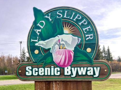 Sign for "Lady Slipper Scenic Byway" featuring a painted lady slipper flower and a sunburst design.