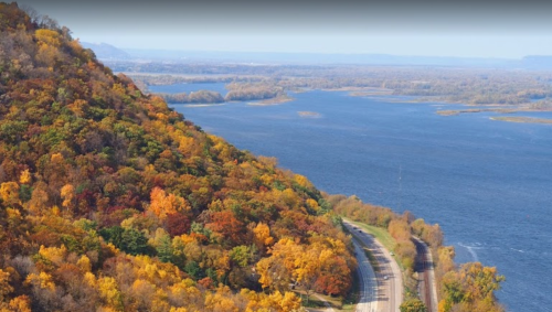 A scenic view of a river surrounded by colorful autumn foliage and a winding road along the water's edge.