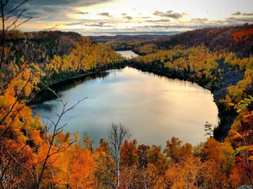 A serene landscape featuring a winding river surrounded by vibrant autumn foliage and a cloudy sky.