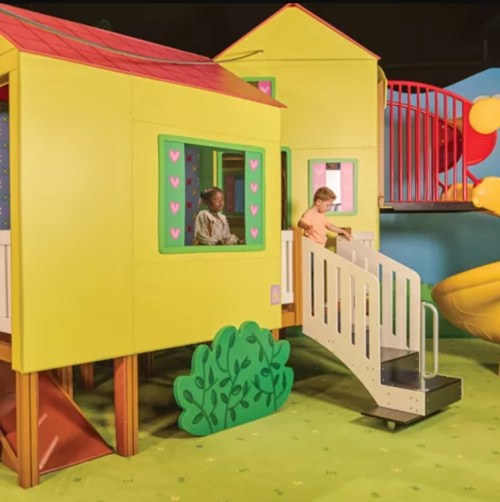 Colorful play structure with a yellow house, slide, and children playing inside and outside.