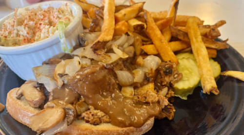 A plate featuring a sandwich with sautéed onions and mushrooms, fries, coleslaw, and pickles.