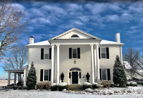 A white two-story house with black shutters, snow-covered ground, and a clear blue sky.