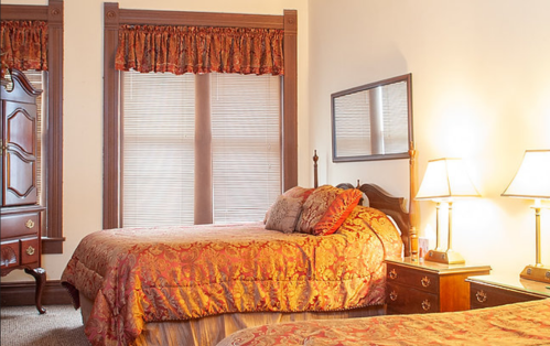 Cozy bedroom with two beds, ornate bedding, wooden furniture, and warm lighting from bedside lamps.