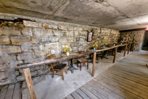 A rustic interior with stone walls, wooden tables, and chairs, adorned with yellow flowers.