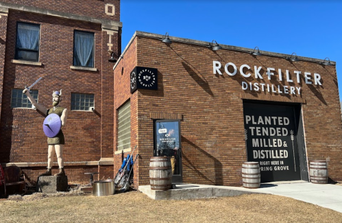 A brick building with "Rock Filter Distillery" sign, featuring a Viking statue outside and barrels nearby.