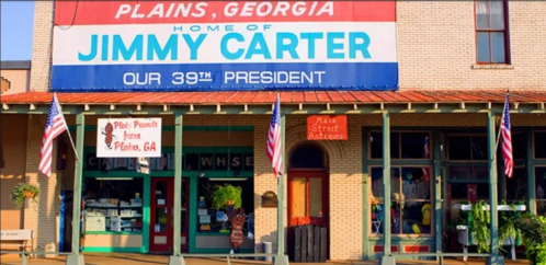 Sign for Plains, Georgia, highlighting it as the home of Jimmy Carter, the 39th President, with storefronts and flags.