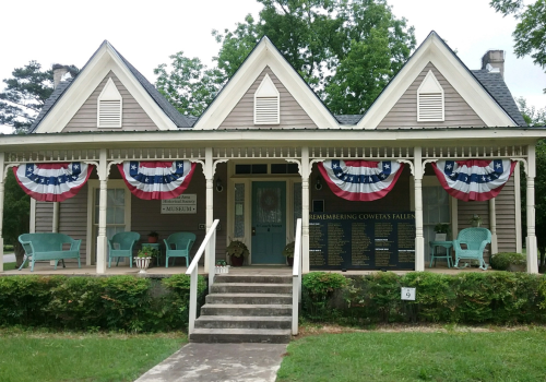 A historic house with a porch, decorated with red, white, and blue bunting, honoring fallen soldiers.