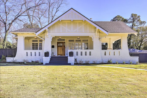 A charming white bungalow with a front porch, surrounded by a well-maintained lawn and trees in the background.