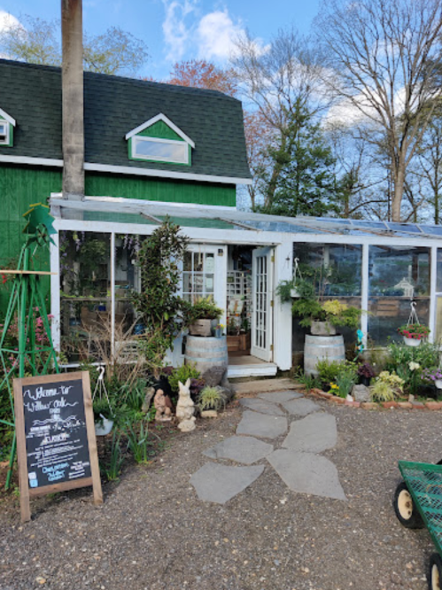 A charming greenhouse with a glass entrance, surrounded by plants and flowers, and a welcome sign in front.