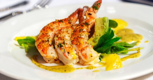A beautifully plated shrimp entree with sauce and fresh avocado.