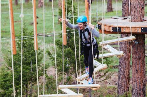 A woman in a blue helmet navigates a rope course, smiling as she steps on wooden planks suspended in the air.