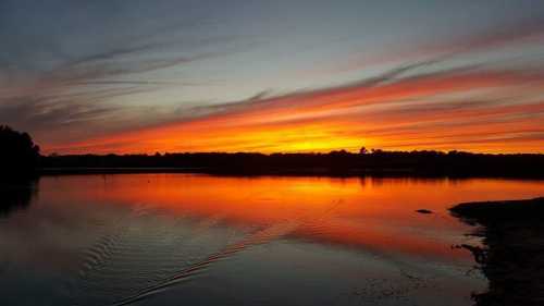 A vibrant sunset over a calm lake, with colorful clouds reflecting on the water's surface.