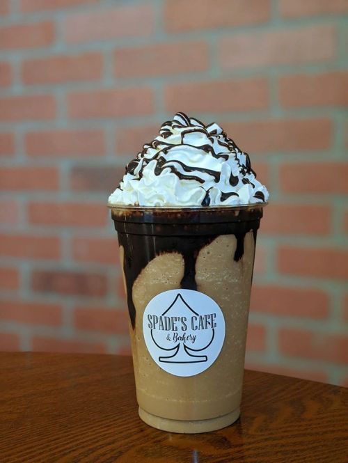 A tall cup of iced coffee topped with whipped cream and chocolate drizzle, featuring a label for Spade's Café & Bakery.