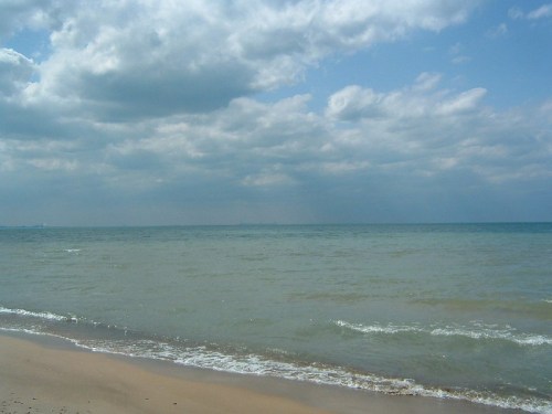 A serene beach scene with gentle waves, sandy shore, and a cloudy sky over the calm ocean.