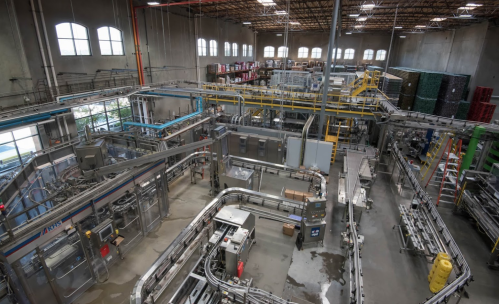 Aerial view of a large industrial facility with machinery, conveyor belts, and storage racks in a spacious environment.