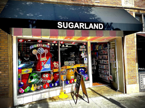 A colorful candy store named "Sugarland" with large candy displays in the windows and a welcoming entrance.