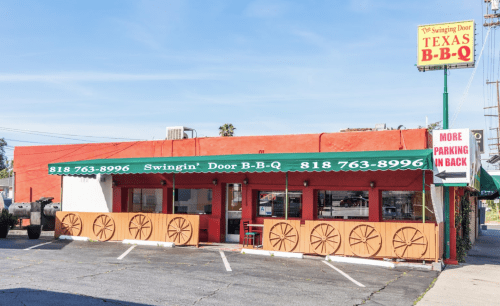 Exterior of Swingin' Door B-B-Q restaurant, featuring a red building, green awning, and a sign for Texas BBQ.