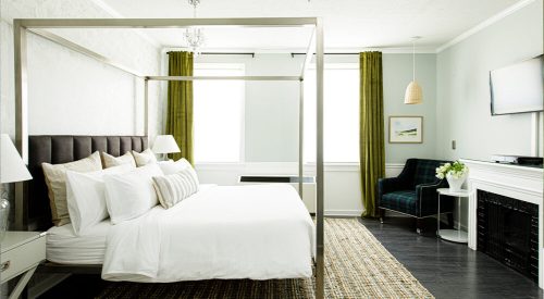 A stylish bedroom featuring a four-poster bed, green curtains, a cozy chair, and modern decor.