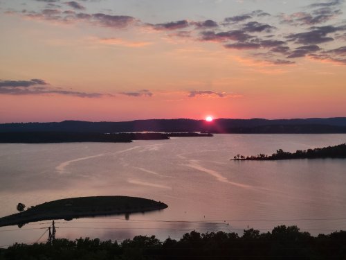 A serene sunset over a calm lake, with silhouettes of hills and clouds reflecting warm colors in the sky.
