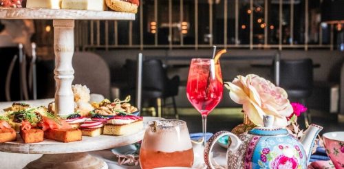 A beautifully arranged afternoon tea set with pastries, a teapot, and colorful drinks on a table in an elegant setting.
