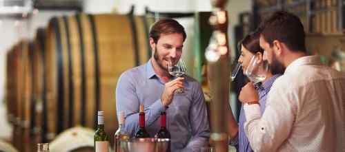 Three people tasting wine in a winery, with barrels in the background and glasses in hand.