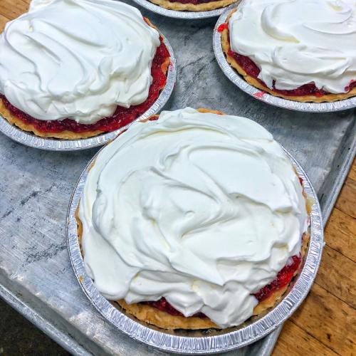 Four cherry pies topped with fluffy whipped cream on a silver tray.