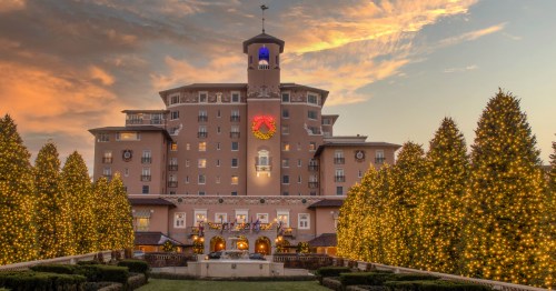 The Broadmoor hotel at sunset, decorated for Christmas with festive wreaths and trees lit by golden lights.