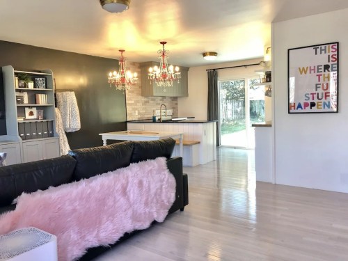 Cozy living space with a black sofa, pink throw, modern kitchen, and colorful wall art. Bright and inviting atmosphere.