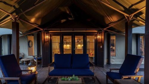 Cozy outdoor seating area with blue chairs and a wooden table, under a tent-like structure, inviting ambiance.