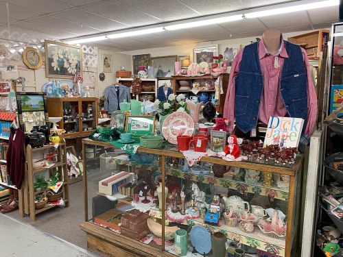 A cozy antique shop filled with vintage items, including dishes, decor, and clothing, displayed in glass cases and on shelves.