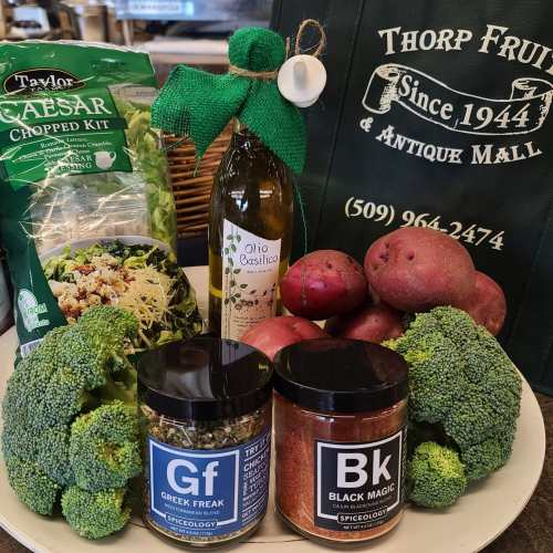A platter with broccoli, potatoes, salad kit, olive oil, and spice jars labeled "Greek Freak" and "Black Magic."