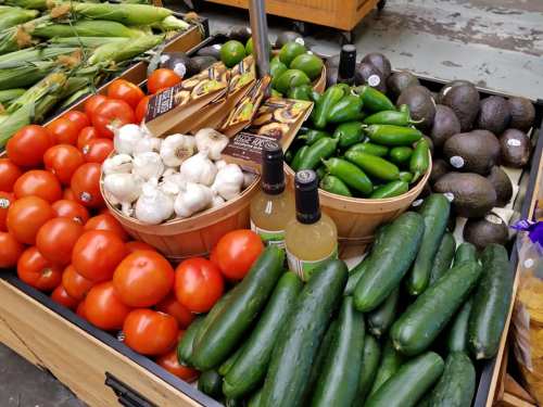 A vibrant display of fresh vegetables, including tomatoes, garlic, jalapeños, avocados, and zucchini at a market.