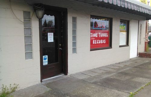 Exterior of a record store named "Time Tunnel Records," featuring a door and large window with colorful signage.