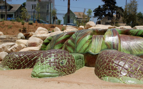 A large, colorful turtle sculpture made of stone, surrounded by rocks and greenery in a park setting.
