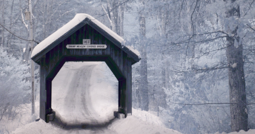 A snow-covered wooden bridge surrounded by frosty trees, creating a serene winter landscape.