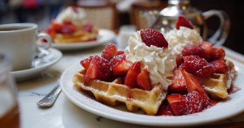 close up of Belgian waffles with strawberries and whipped cream at a table at a cafe outside next to coffee cups
