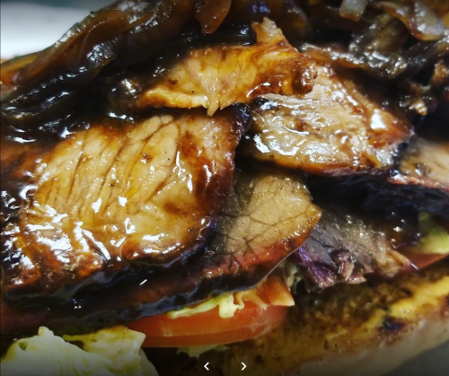 Close-up of a sandwich filled with layers of tender, glazed beef, topped with onions and served on a toasted bun.